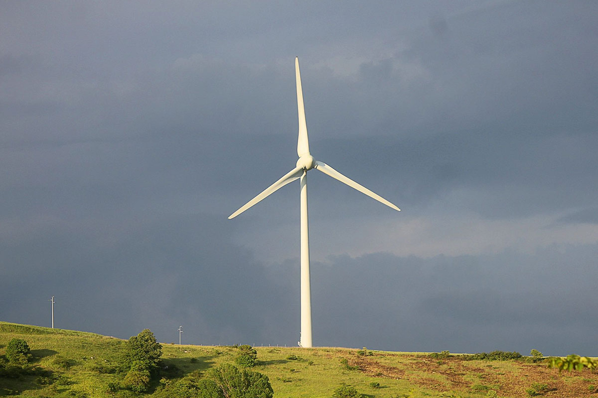 A wind turbine on top of a hill with trees in the background.